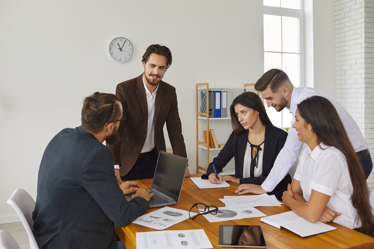 Cross-functional offshore software team collaborating in a meeting around a table with laptops and documents, illustrating productivity ramp-up, structured onboarding, and team performance growth.
