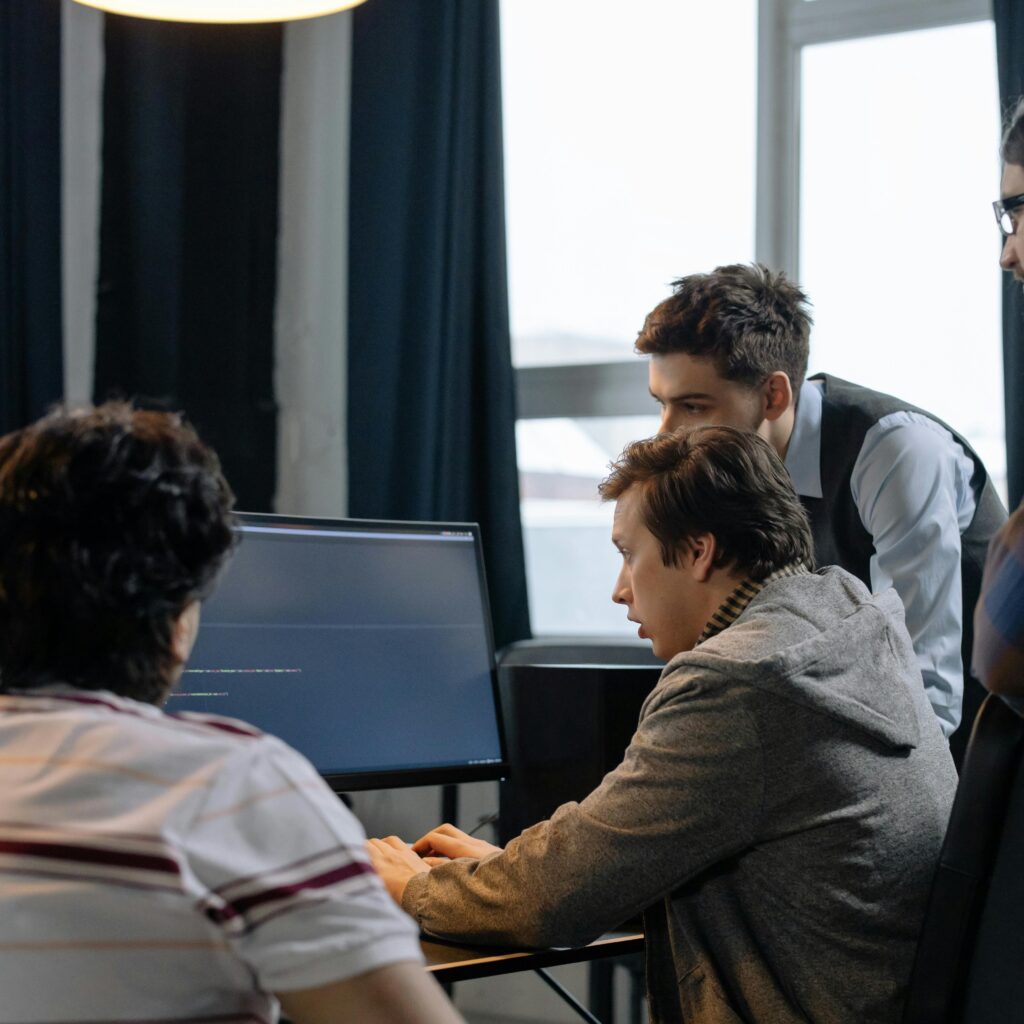 Software development team collaborating around a computer screen, discussing code and project strategy, representing offshore engineering teams, collaboration, and high-performance software development.
